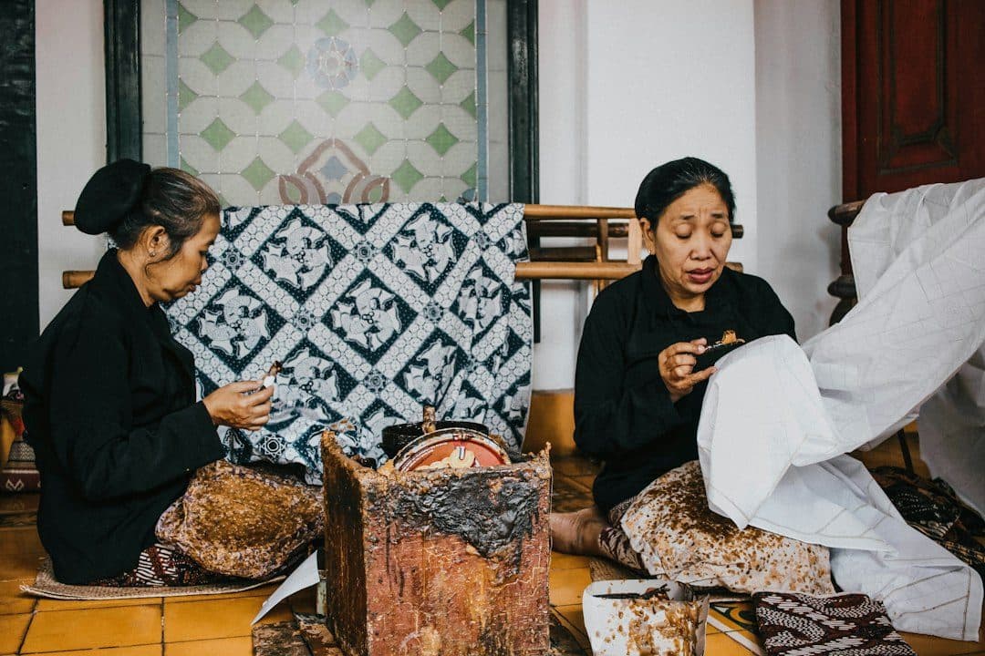 Perajin membatik dengan canting di depan kain batik