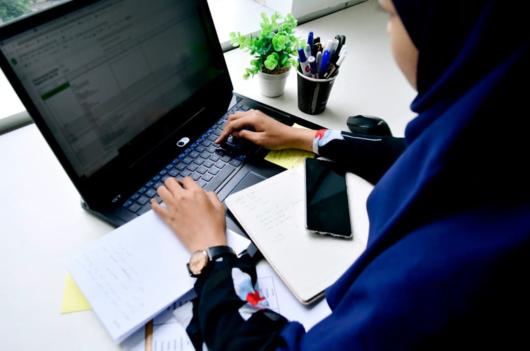 Perempuan berhijab bekerja dengan laptop dan buku catatan di meja